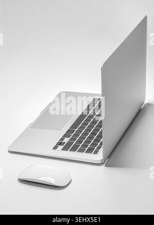 A sleek silver laptop and a white wireless mouse are positioned on a white surface. Stock Photo