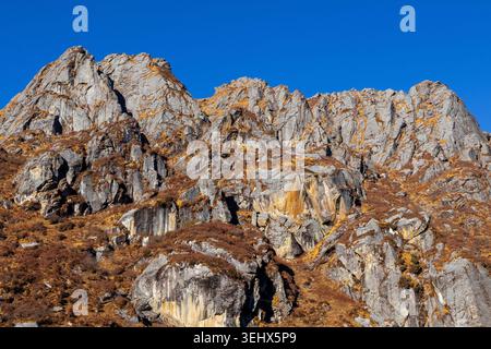 Rugged rocky mountain cliffs with dry golden grass under a clear blue sky. Stock Photo