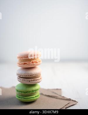three pastel macarons stacked on torn kraft paper in a minimalist bright studio table setup; soft natural light emphasizes delicate shells, creamy fil Stock Photo