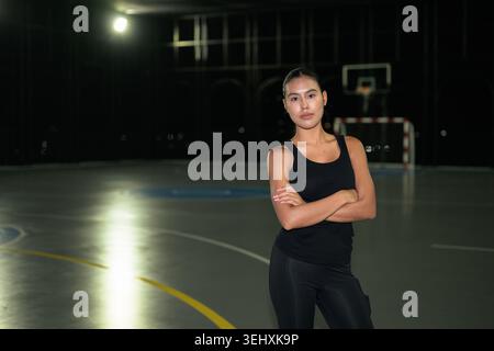 A professional horizontal medium shot of a focused and fit young Asian Thai woman posing with her arms crossed on an outdoor multi-purpose sports cour Stock Photo