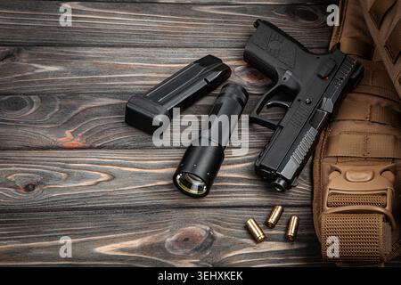 Tactical handgun with a magazine, flashlight, and ammo on a dark wooden background. Stock Photo