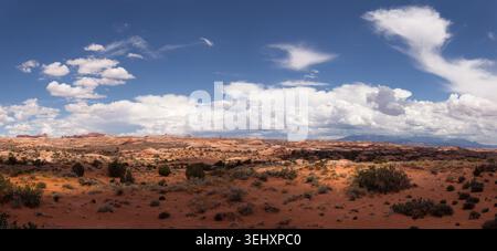 A wide panoramic desert landscape featuring sweeping red rock flats and distant plateaus under a crisp blue sky with scattered clouds Stock Photo