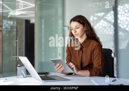 Businesswoman concentrating on tablet and laptop at a modern office desk, multitasking between data, planning and online tools to boost productivity in a professional workspace Stock Photo
