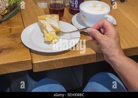 A piece of apple cake next to a cup of coffee on a wooden table, held by one hand in a cozy atmosphere, Cafe Kuh, Deckenpfronn, Germany Stock Photo