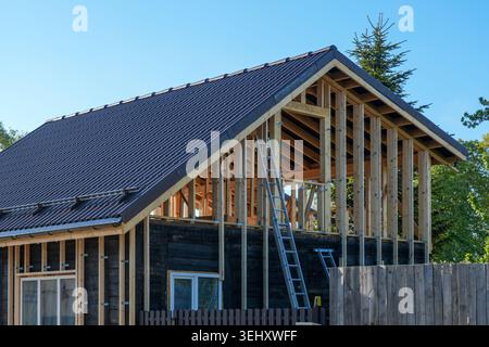 Residential timber frame house under reconstruction with exposed wooden structure and finished tiled roof Stock Photo
