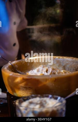 A chef prepares pasta by mixing it in a cheese wheel Stock Photo