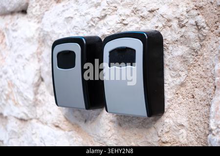 Close up of two outdoor key lock boxes with combination locks, securely mounted on a rustic stone wall for vacation house access. Stock Photo