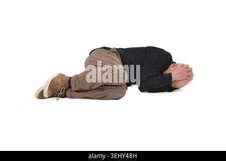 front view of  man lying on the ground in the fetal position, covering his face Stock Photo