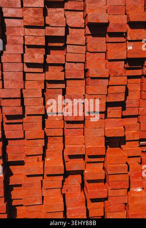 Bricks are stacked tightly in a construction area during the day. The uniform arrangement shows many bricks in red color, waiting to be used for build Stock Photo