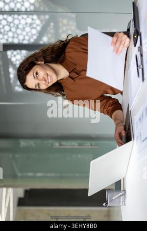 Smiling Hispanic businesswoman sitting at her office desk workspace, typing on a laptop computer and focusing on her daily corporate tasks and management. Stock Photo