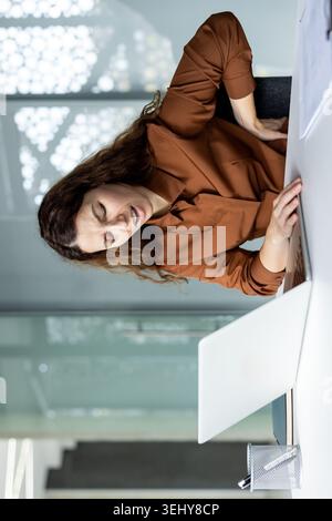 Modern Hispanic female entrepreneur using a digital tablet computer, scrolling on the touch screen and analyzing data or presentation at her office workplace. Stock Photo