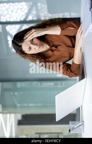 Serious Latina female manager holding a clipboard and writing notes, conducting an audit, checking a checklist or inspecting reports at her office desk. Stock Photo