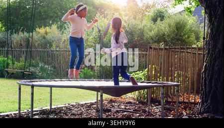Trampoline, jumping and children in backyard for fun, playing and bonding together on weekend. Happy, development and girl kids on bouncing playground Stock Photo