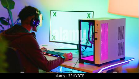 Gamer, computer screen and teen with headphones in home for esports competition, action and back. Headset, boy and gaming monitor for gameplay Stock Photo