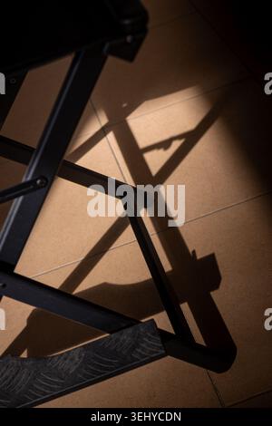 Chair creating abstract geometric shadows on a warm brown tiled floor, highlighting contrast and minimalist composition Stock Photo