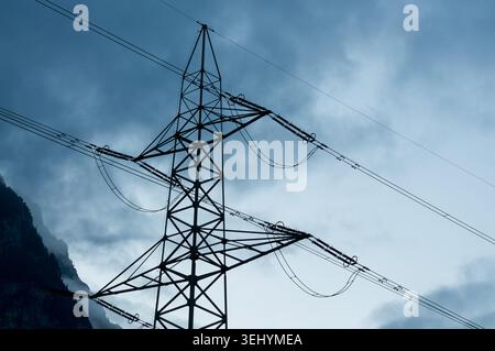 Low angle symmetric view of a high voltage electricity pylon or powerline tower. Geometric steel framework construction against dramatic blue sky, con Stock Photo