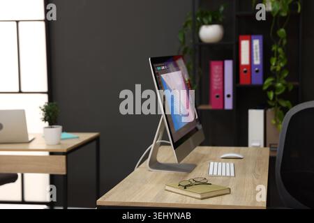 Wooden desks with computers, stationery, plants and shelving unit in office. Interior design Stock Photo