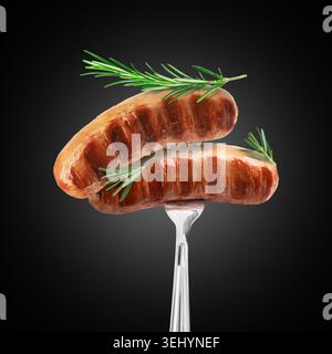 Delicious grilled meat sausages with rosemary on fork against black gradient background Stock Photo