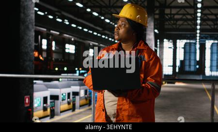 Black engineer with hard hat surveys the machinery hall ensuring safety and productivity standards, heavy industry plant showcases steel construction on large-scale equipment industrial design. Stock Photo
