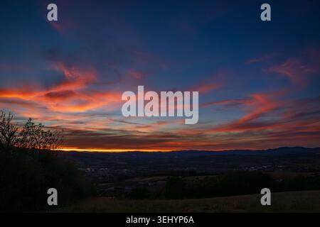 A spectacular sunset paints the sky over the Beaujolais hills. Intense shades of orange and red ignite the wispy clouds, which contrast with the deep Stock Photo