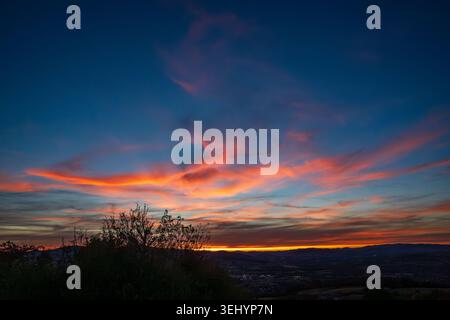 A magnificent twilight sky ignites with vibrant orange and red hues over Beaujolais. Wind-swept clouds create dynamic shapes in the deep blue, while t Stock Photo