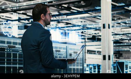 Writing code, laptop program and software developer in data center doing resource optimization. Upgrading IT infrastructure, programming script on notebook worker walking in server hub, camera B Stock Photo