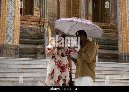 BANGKOK, THAILAND-MAY 16, 2026: Tourist couple holding umbrella and using smartphone together, mobile work lifestyle, front view Stock Photo