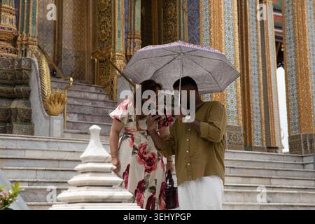 BANGKOK, THAILAND-MAY 16, 2026: Tourist couple holding umbrella and using smartphone together, personal moment with phone, front view Stock Photo