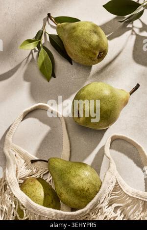 Overhead flat lay shot of fresh, vibrant green Italian pears inside a reusable eco-friendly woven mesh string bag. The bag rests on a kitchen table ca Stock Photo
