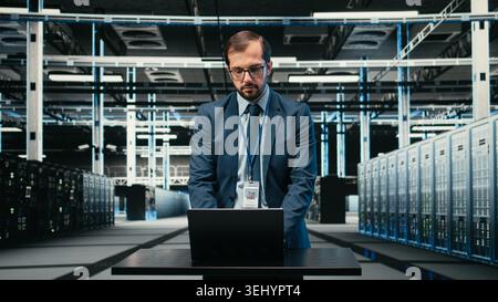 Data center technician using laptop and augmented reality to install upgraded server racks systems. Worker using automation tools to monitor server farm performance, VFX overlay, camera A Stock Photo