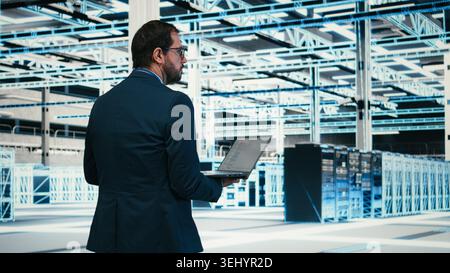 Writing code, laptop program and software developer in data center doing resource optimization. Upgrading IT infrastructure, programming script on notebook worker walking in server hub, camera A Stock Photo