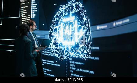 Engineering team looks at AI machine learning self writing code on screen, autonomy concept. Teamworking colleagues reviewing self sustaining artificial intelligence model, doing brainstorming Stock Photo