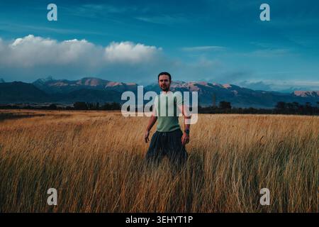 Portrait of a young man standing in tall dry grass with mountain landscape in the background in Kyrgyzstan. Stock Photo