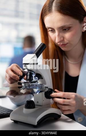 Close up of female technician in microchip factory RD office analyzing microelectronic circuits with lab microscope. Expert inspecting PCB hardware parts with optical equipment in research facility Stock Photo