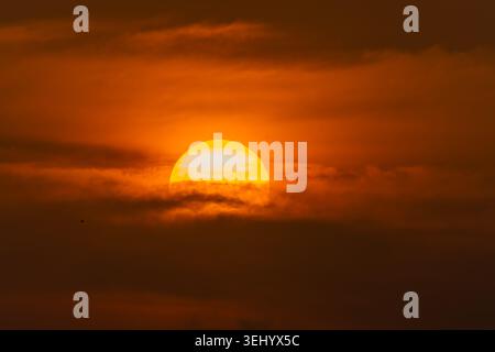View of a large glowing sun setting behind dark atmospheric clouds in an orange sky Male, Male, Maldives. Stock Photo