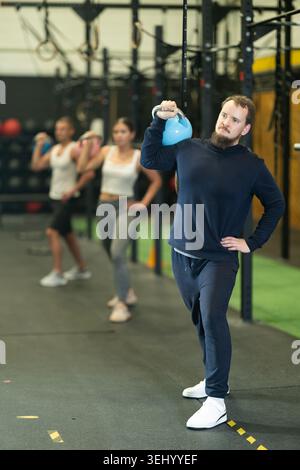 Bearded man doing kettlebell overhead shoulder press in gym Stock Photo