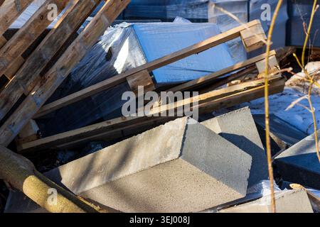 Fallen grey concrete blocks stacked on wooden pallets wrapped in plastic film, construction site waste, debris scattered outdoors in winter sunlight d Stock Photo