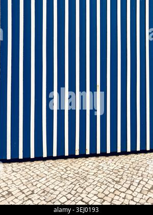 A vertical shot featuring a geometric pattern of vibrant blue and white painted wooden slats positioned above a textured light colored stone cobblesto Stock Photo