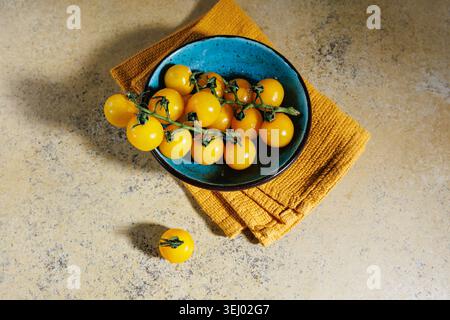 Bright heirloom tomatoes in blue bowl on rustic yellow towel Stock Photo