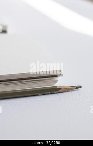 Sharpened pencil and notebook pages on white surface in studio close up. Minimal stationery, creative office, modern productivity, elegant branding Stock Photo