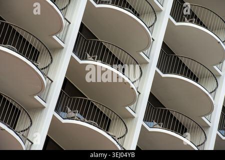 Modern building with curved balconies and metal railings. White concrete structure curves upward in layered fashion. Repeating geometric shapes. Stock Photo