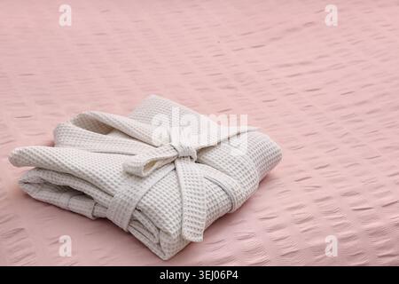 Folded waffle bathrobe on pink blanket in bedroom Stock Photo