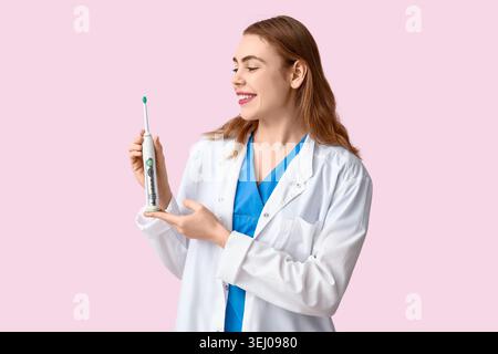 Female dentist showing electric toothbrush on pink background. World Dentist Day Stock Photo