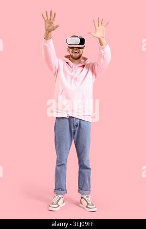 Young bearded man using VR glasses on pink background Stock Photo