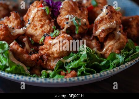Close-up of a dish of breaded fish or shrimp on fresh lettuce with spicy chipotle cream on top, inside a bowl. Stock Photo