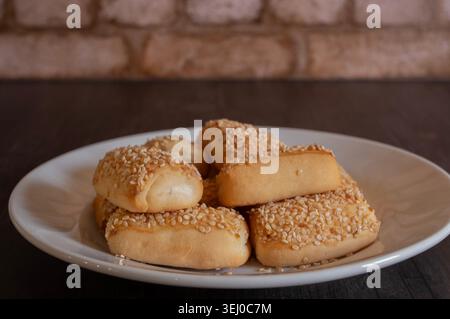 Small rolls or buns filled with cream cheese and topped with sesame seeds, on a white plate with a brick wall in the background; foods to accompany pr Stock Photo