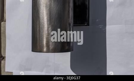 Brushed wall light fixture mounted on a surface with white paper backdrop, showcasing metallic finish and shadow details in a well-lit environment Stock Photo