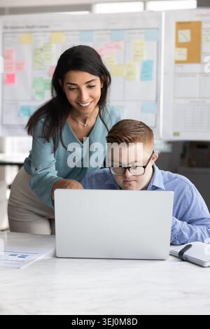 Coworker helping young man with Down syndrome in office Stock Photo