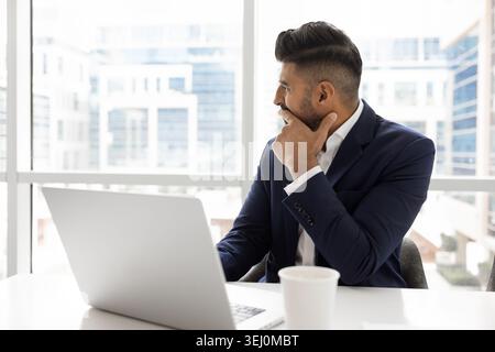 Businessman looking out window seated at desk with laptop Stock Photo