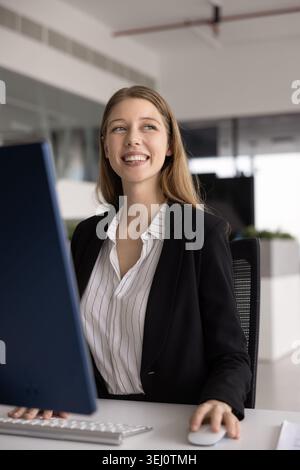 Young professional woman sits in workplace desk with computer Stock Photo